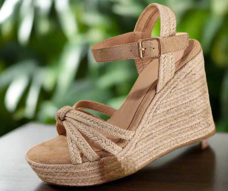Beige wedge sandal with braided design held by a hand against a neutral background