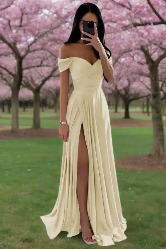 Pale yellow off shoulder satin gown with pleated A-line skirt and high slit, styled for spring weddings or garden parties.