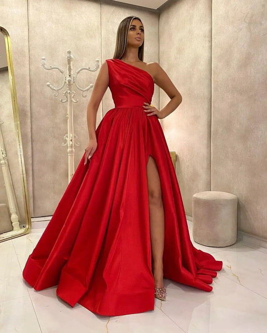 Woman wearing a red one-shoulder gown with a slit in a stylish interior setting.