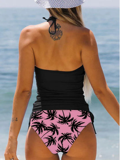 Woman wearing a black top and pink high-waisted bikini bottom with palm tree pattern by the ocean.
